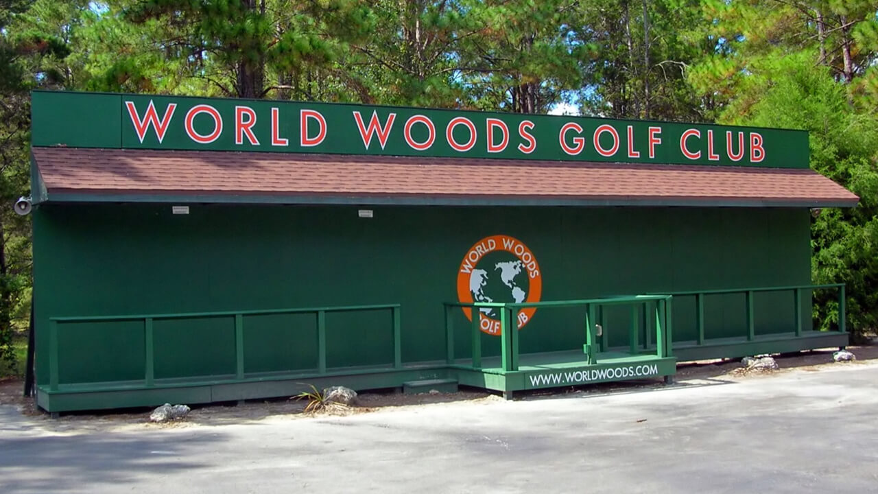 A green panel with the words "World Woods Golf Club" stands against a group of trees. 