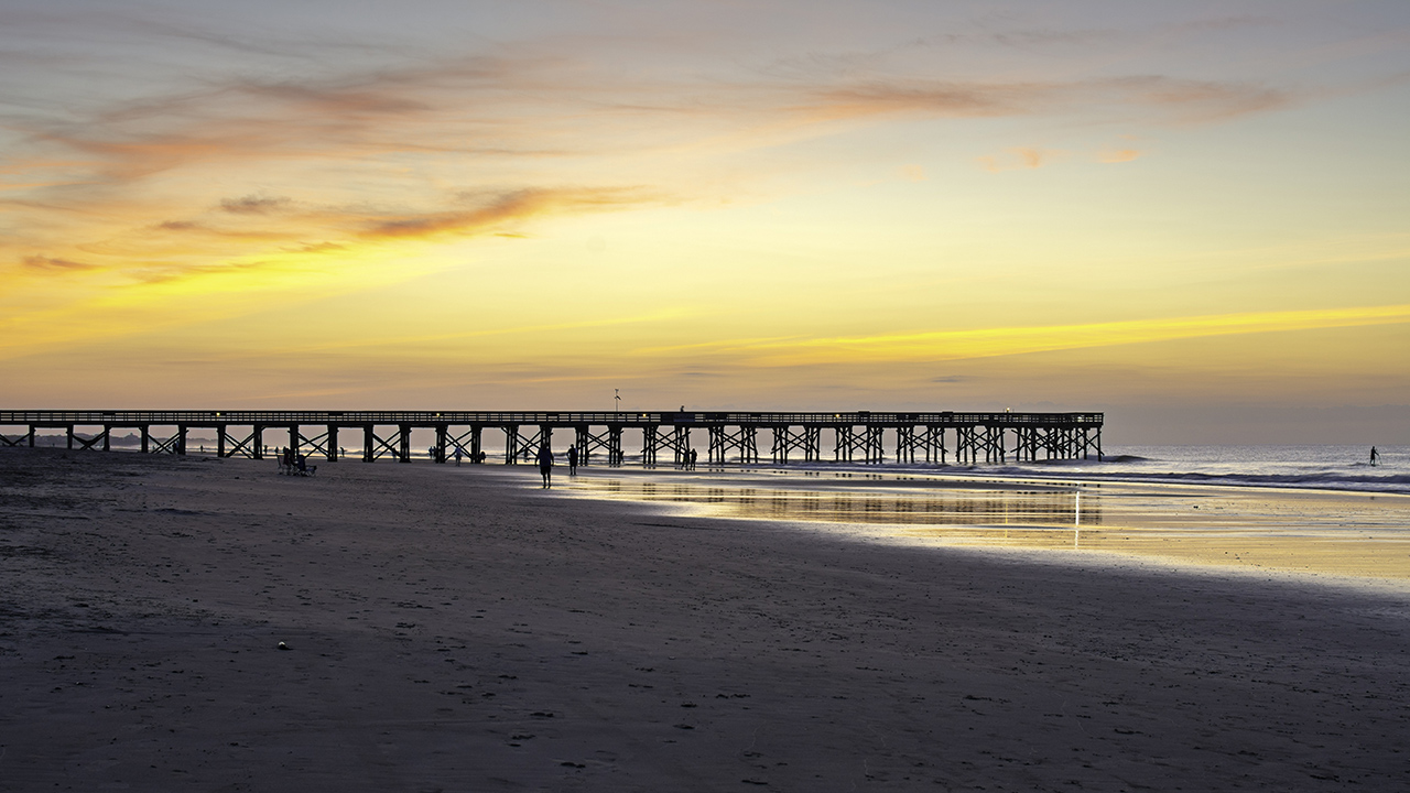 The Isle of Palms' beach boardwalk stretches out into the ocean during sunset in South Carolina. 