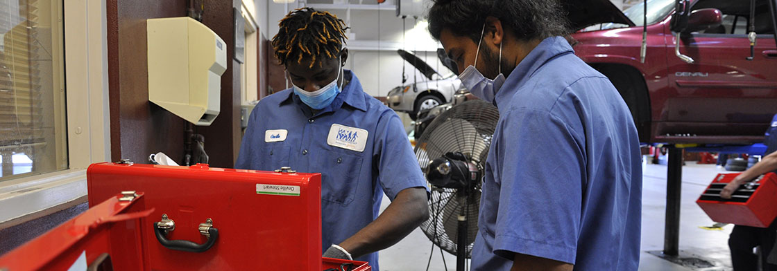 Two YATC students search through a red toolbox in a vehicle repair garage. 