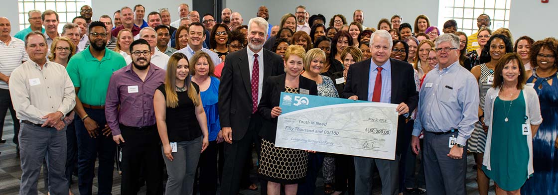 Dozens of associates gather around a giant cardboard check written to Youth In Need for $50,000. 
