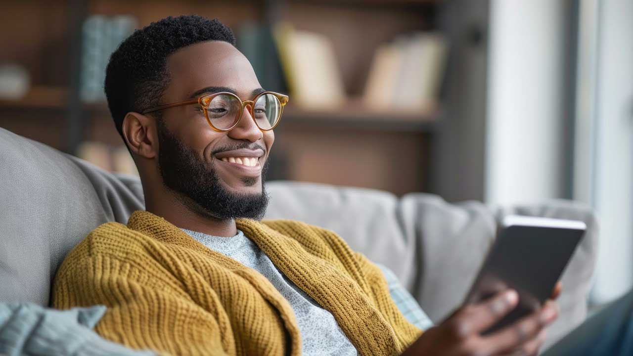 Adult male in yellow sweater smiling and checking ipad
