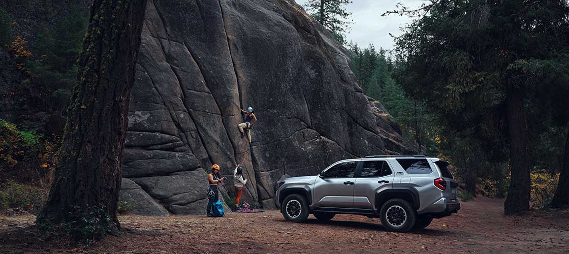 A silver 2025 Toyota 4Runner facing a cliff as mountain climbers scale a wall