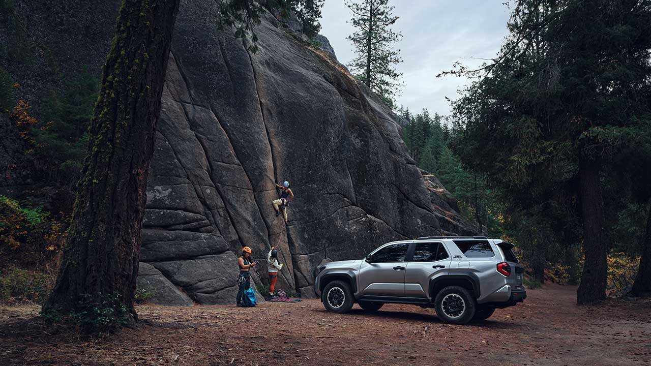 A silver 2025 Toyota 4Runner facing a cliff as mountain climbers scale a wall