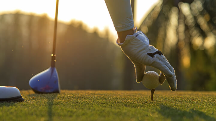 A gloved hand places a golf ball on a tee.