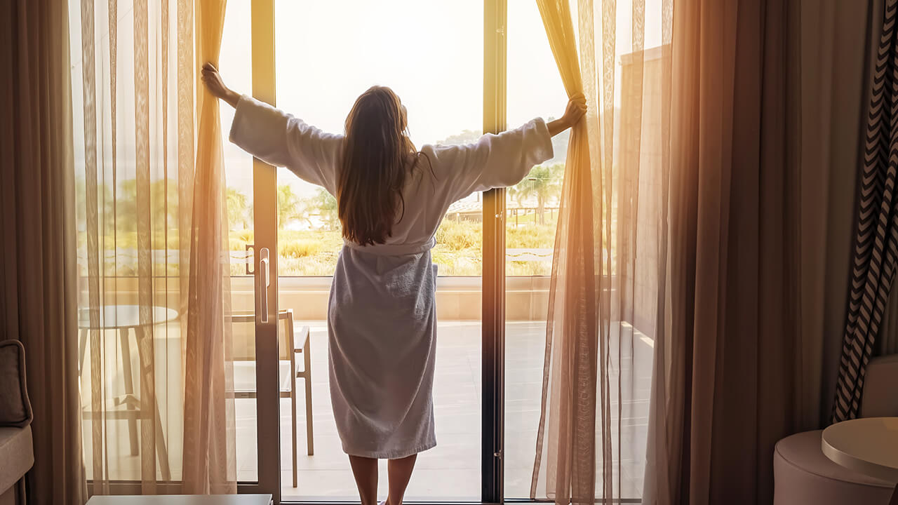 Woman in bathrobe opening hotel window curtains