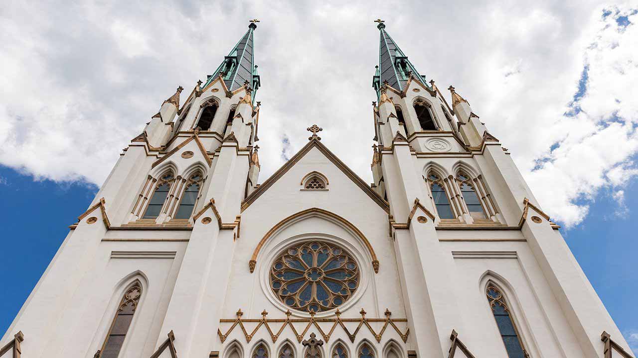 Two spires of the Cathedral Basilica of St. John the Baptist press against a cloudy blue sky.