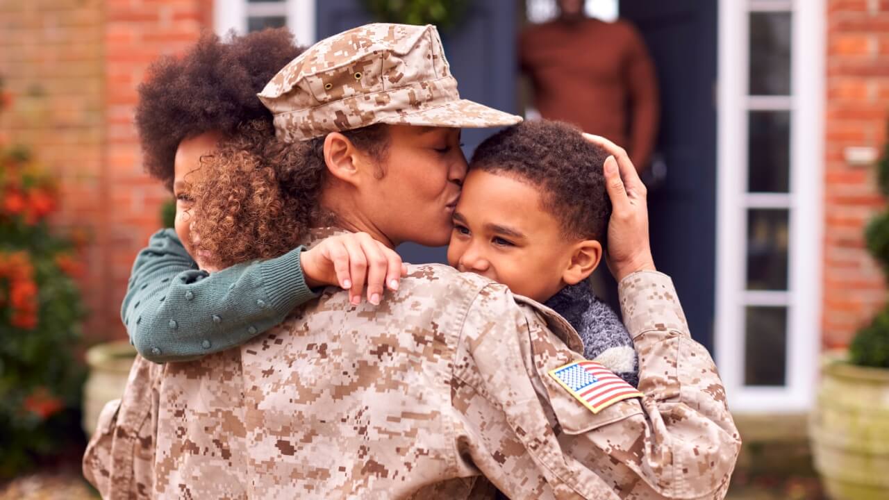 Mother in military fatigues hugging children